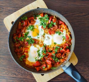 szakszuka z pomidorami i papryką, podana na patelni.