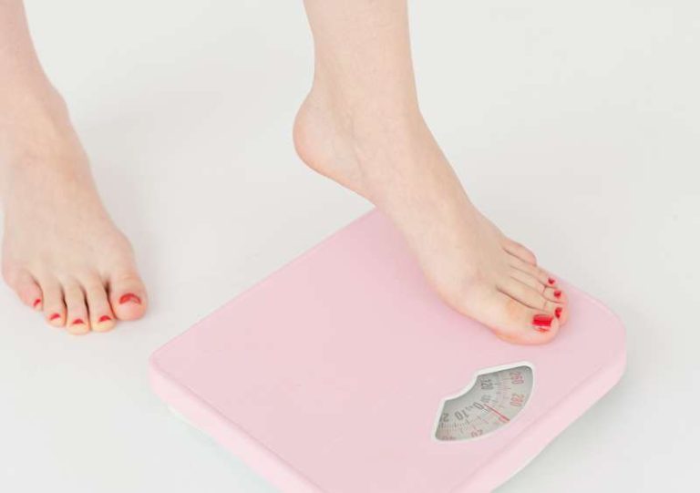 Kobieta wchodzi na różową wagę łazienkową