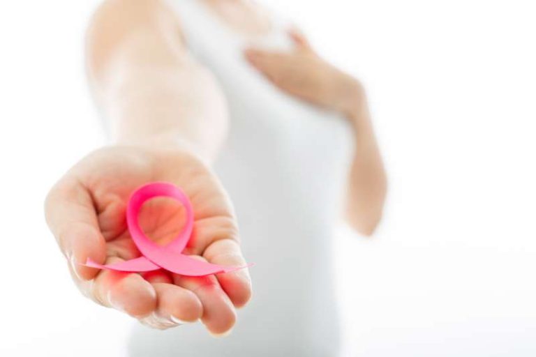 Kobieta trzyma wyciągniętą dłoń. Na dłoni różowa wstążka - symbol profilaktyki raka piersi