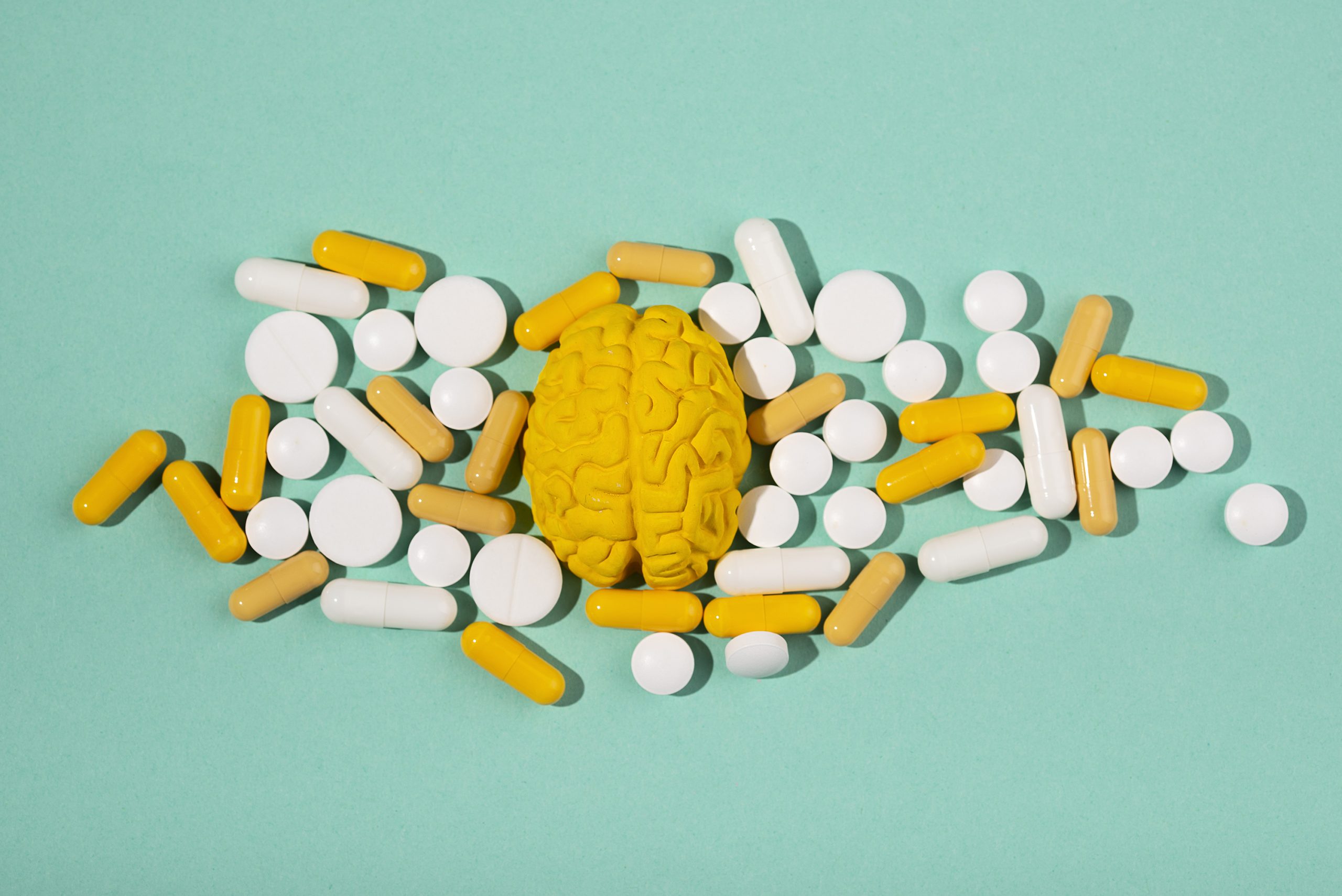 Mózg i tabletki Żółty model mózgu otoczony białymi i żółtymi tabletkami na turkusowym tle.