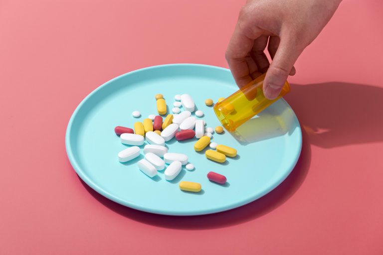 Kolorowe tabletki na niebiskim talerzu wysypane z pojemnika na różowym tle