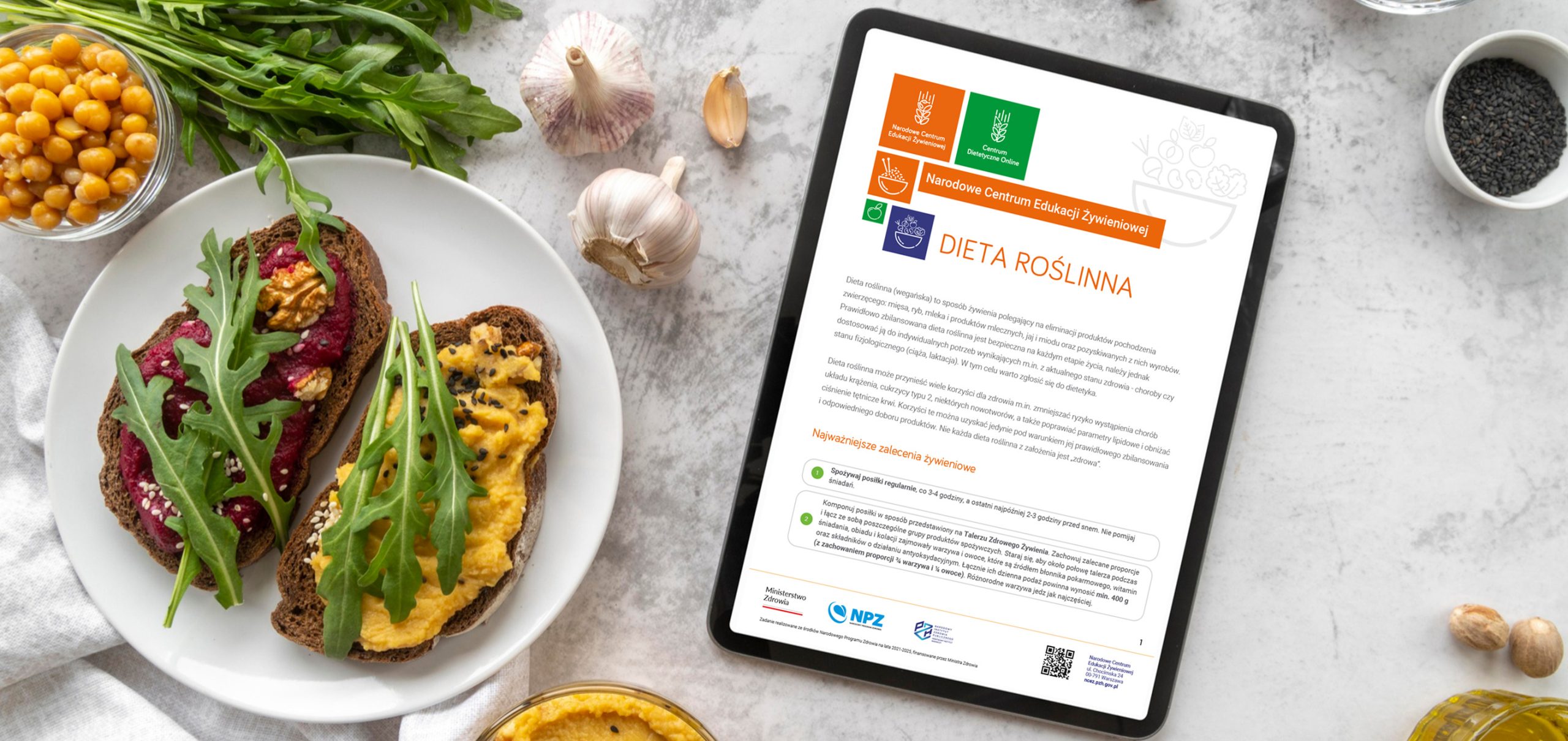 Tablet z zaleceniami żywieniowymi na stole, obok talerz z dwiema kanapkami z pastą wegetariańską.