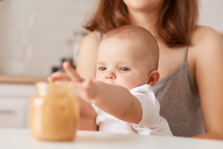 Małe dziecko na kolanach matki sięgające rączką do słoika z jedzeniem